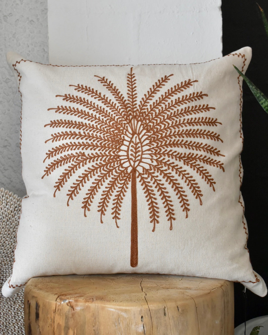 Decorative pillow with brown tree design on a white background, placed on a wooden block.