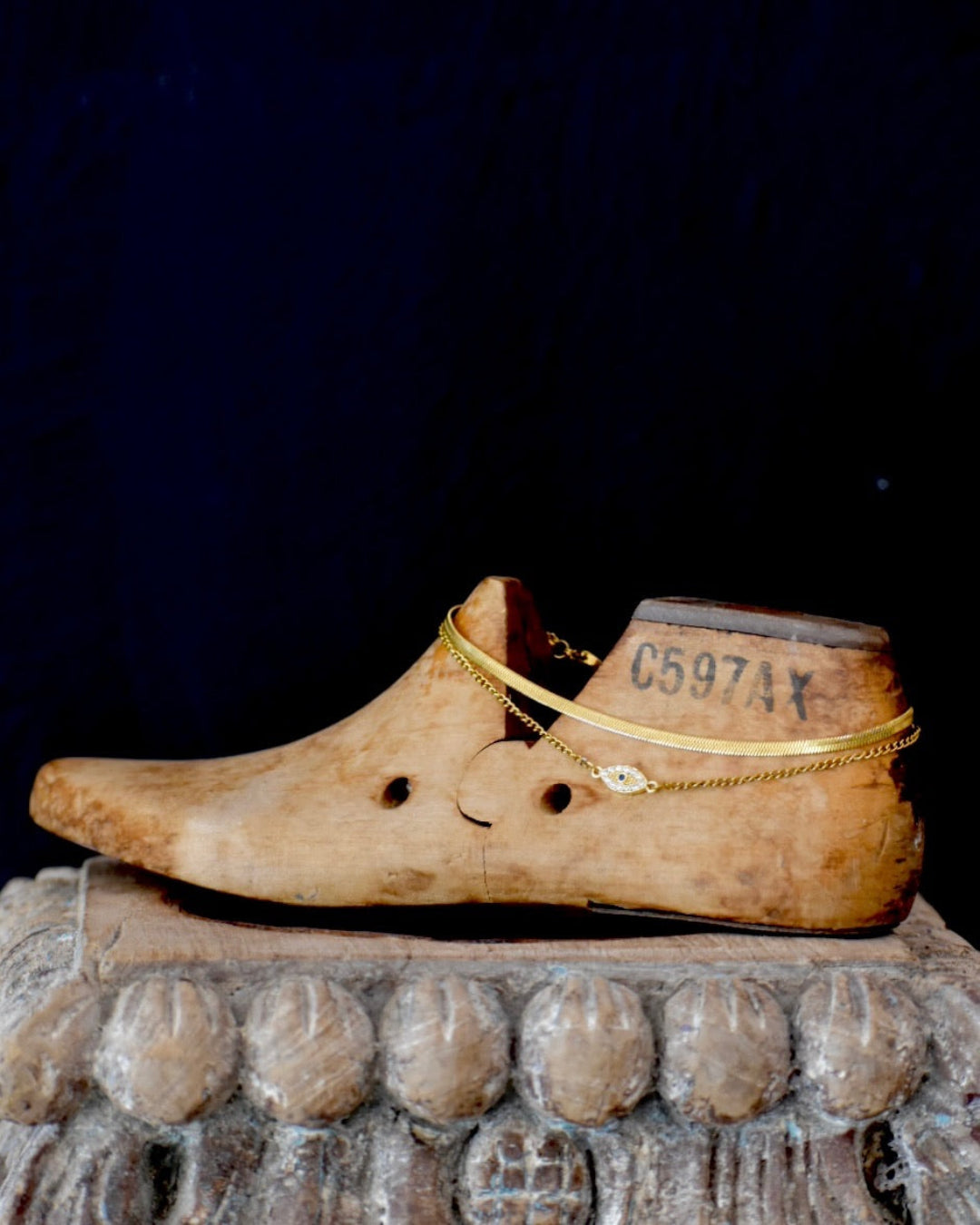 Wooden shoe with a gold evil eye anklet chain on a decorative candle holder