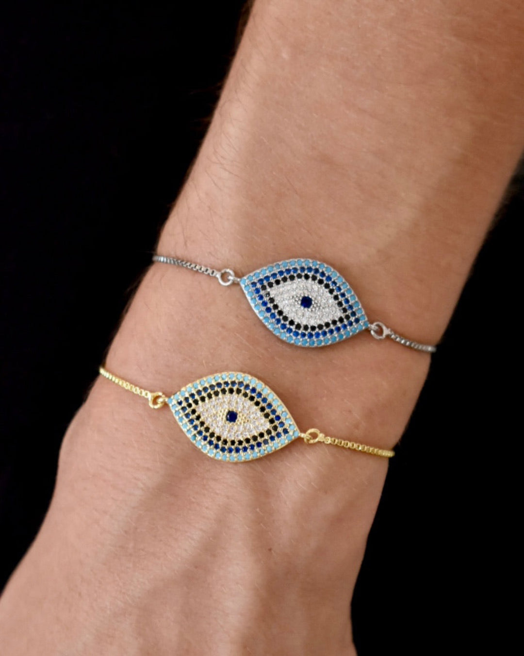 Two eye-shaped bracelets on a wrist against a black background