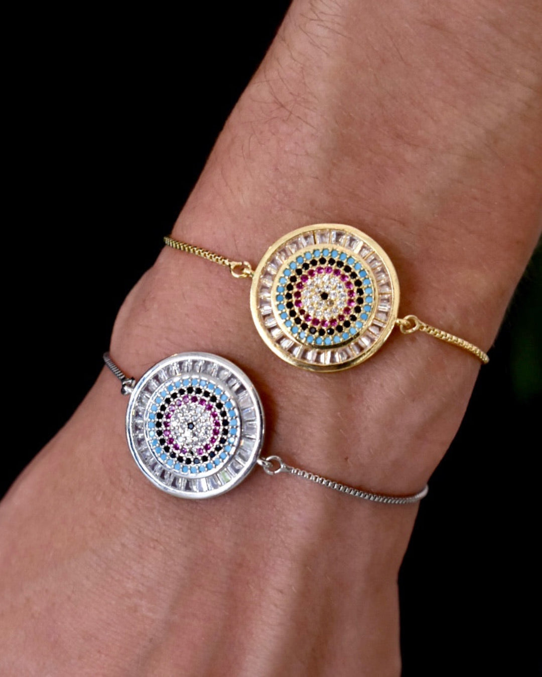 Two circular bracelets with colorful gemstones on a wrist against a black background