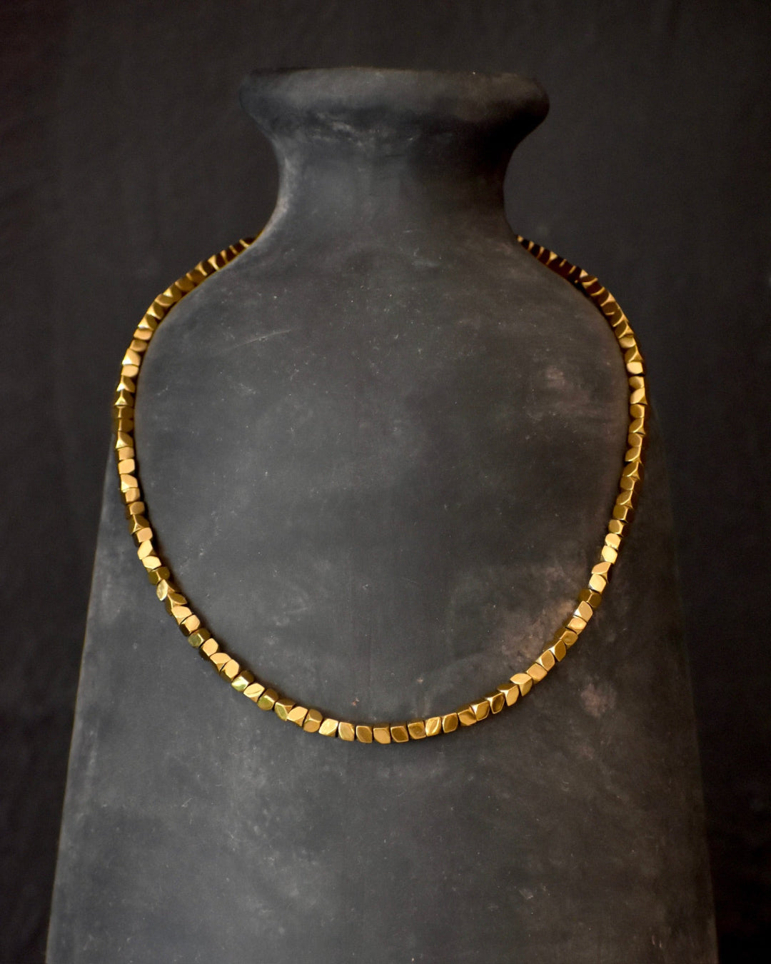 Gold necklace on a black mannequin bust against a dark background
