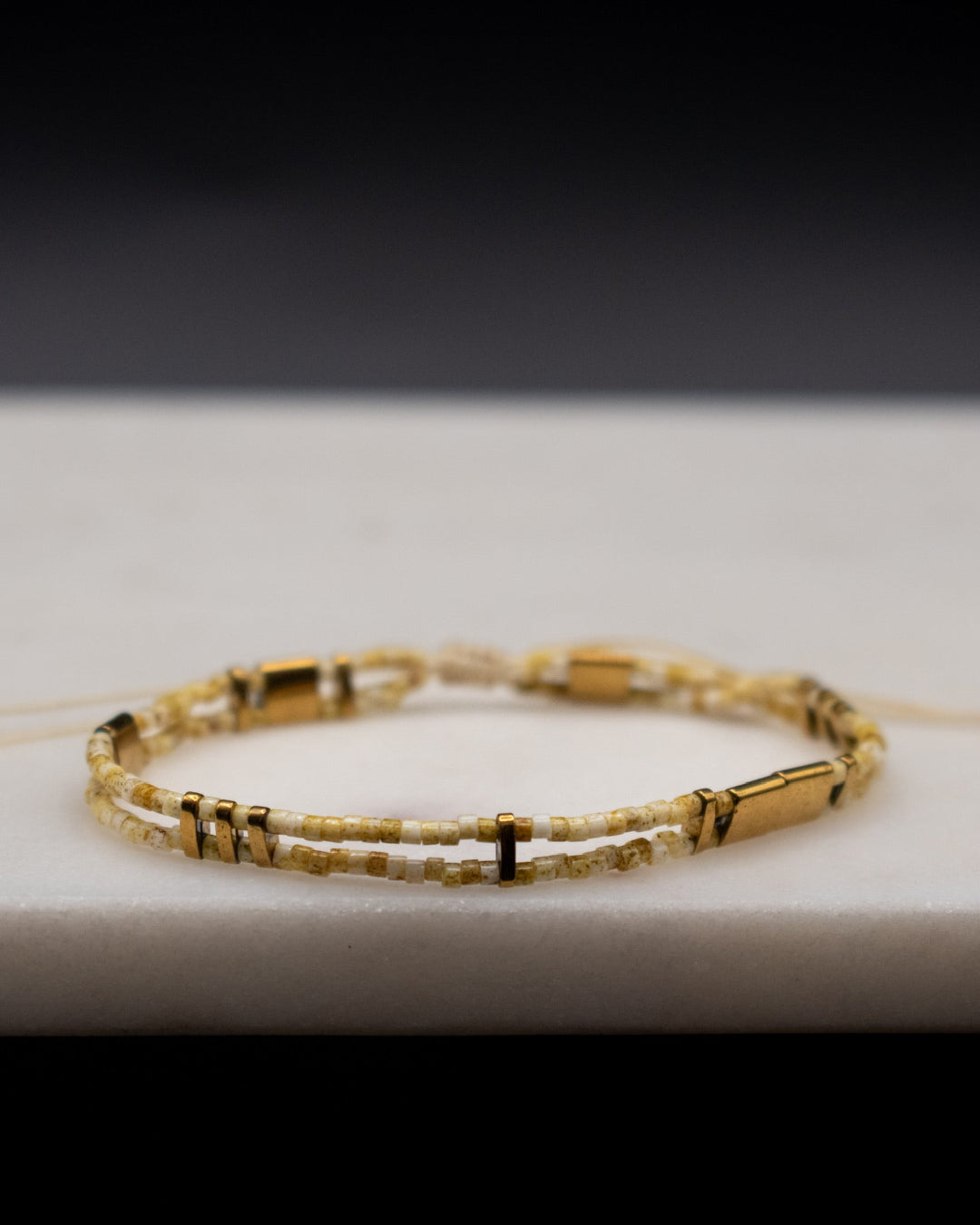 Gold beaded bracelet on a white surface with a dark background