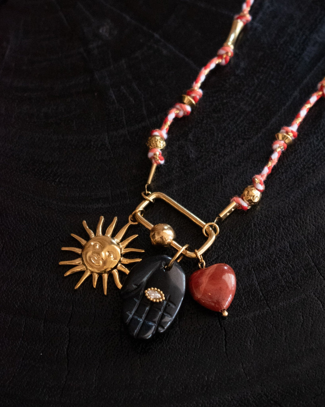 Necklace with sun, hand, and heart charms on a dark background
