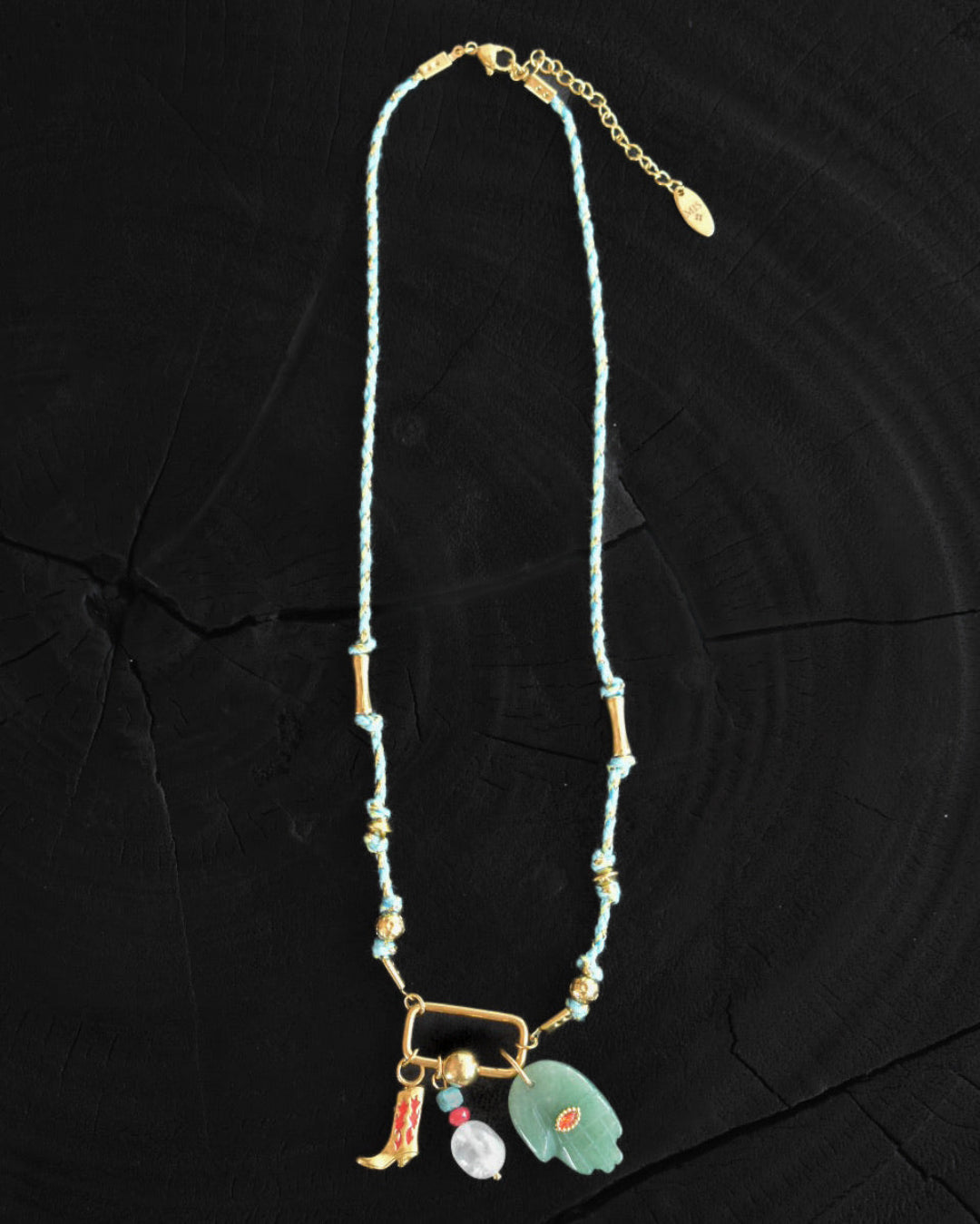 Necklace with cowboy boot and hand pendants on a dark textured surface