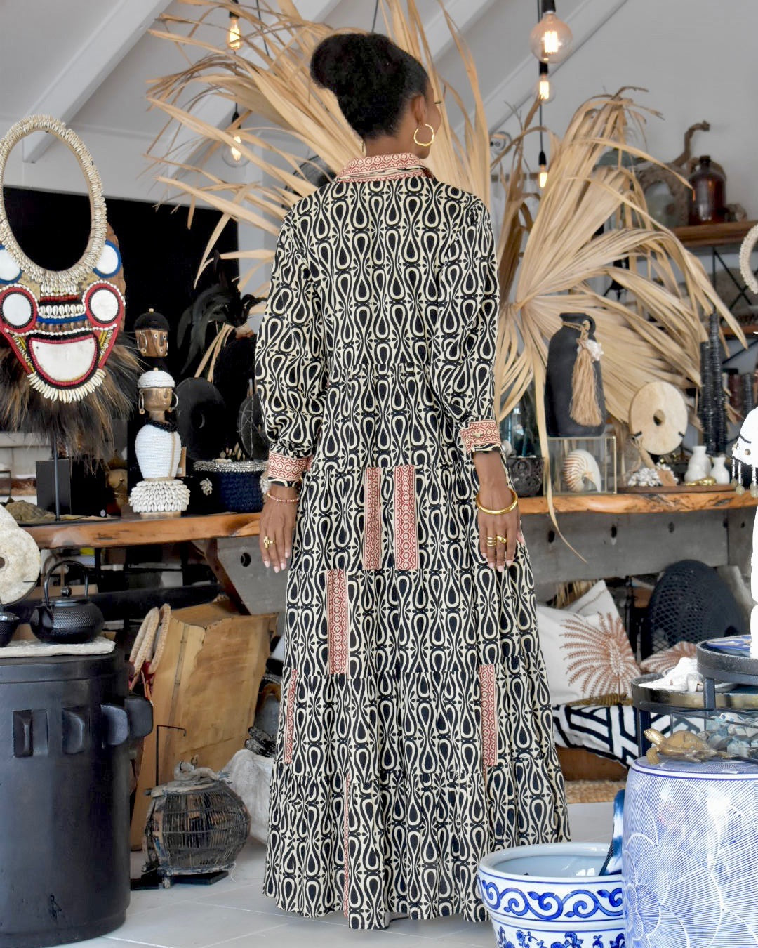 Woman in a patterned dress standing in a store with various decorative items around her.