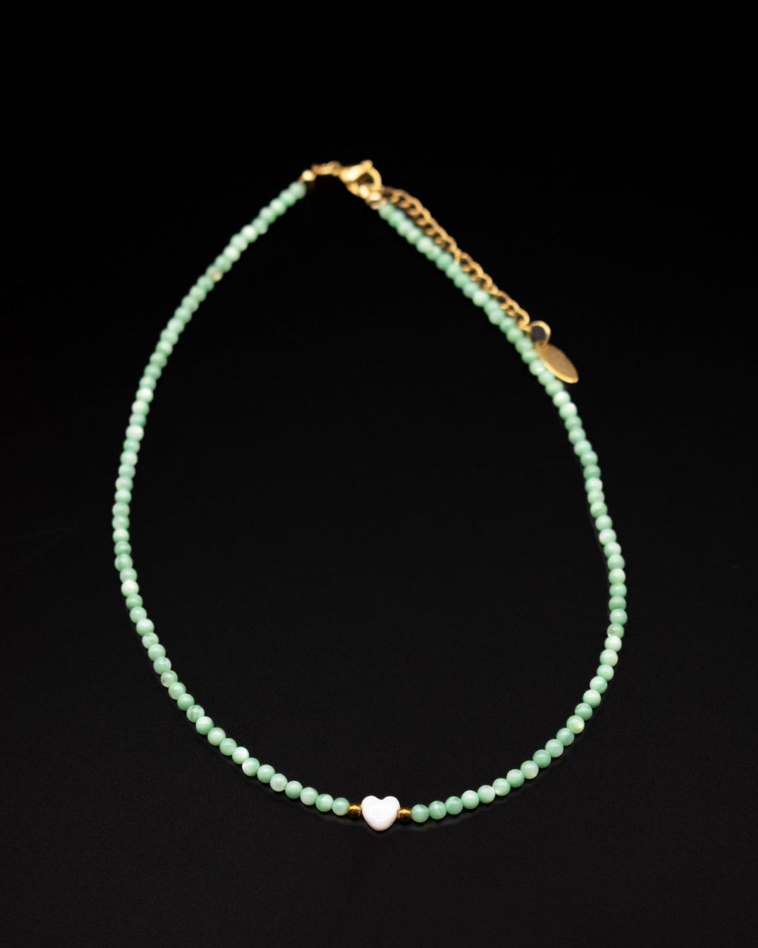 Green beaded necklace with a heart charm on a black background