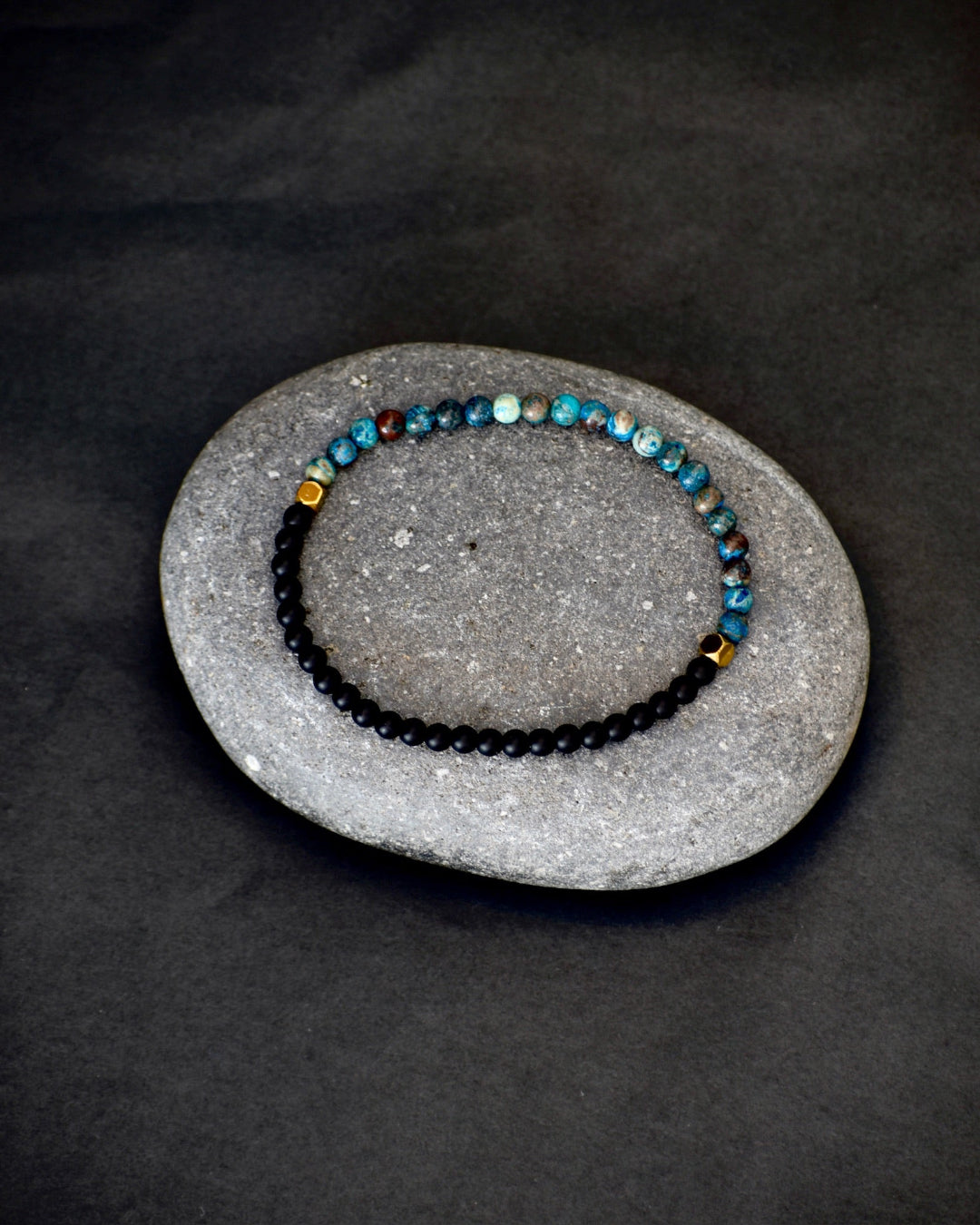 Two beaded bracelets on a gray stone surface with a dark background