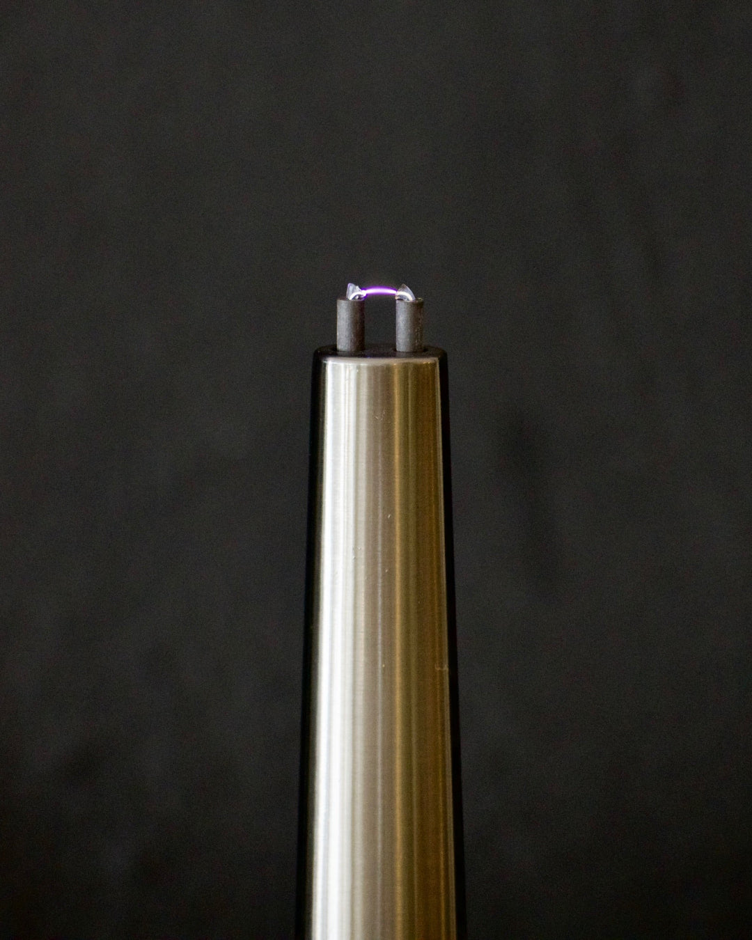 Metallic object with a glowing purple tip against a dark background