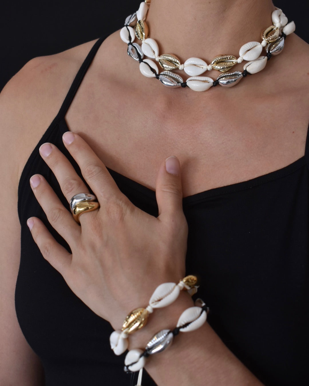 Necklace, bracelet, and ring with shell-like design worn by a person on a black background