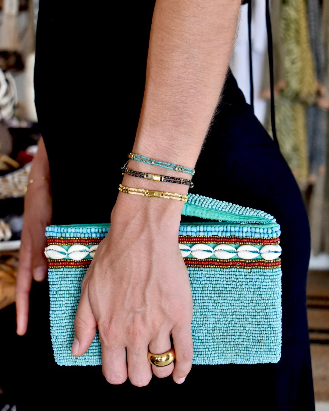 Turquoise beaded clutch held by a person with gold rings and bracelets.