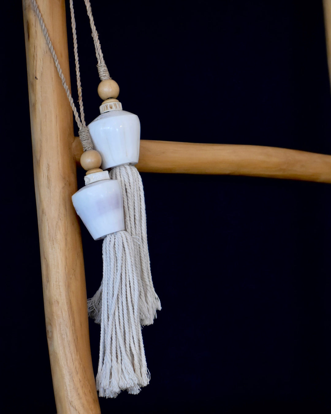 Decorative tassel with white ceramic beads on a wooden stick against a black background