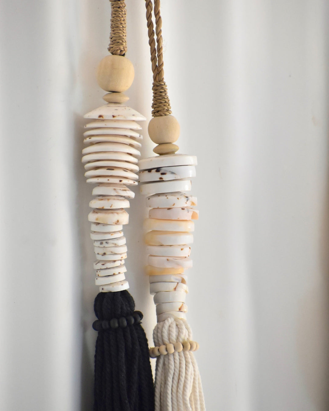 Decorative hanging with shell beads and tassels on a plain background