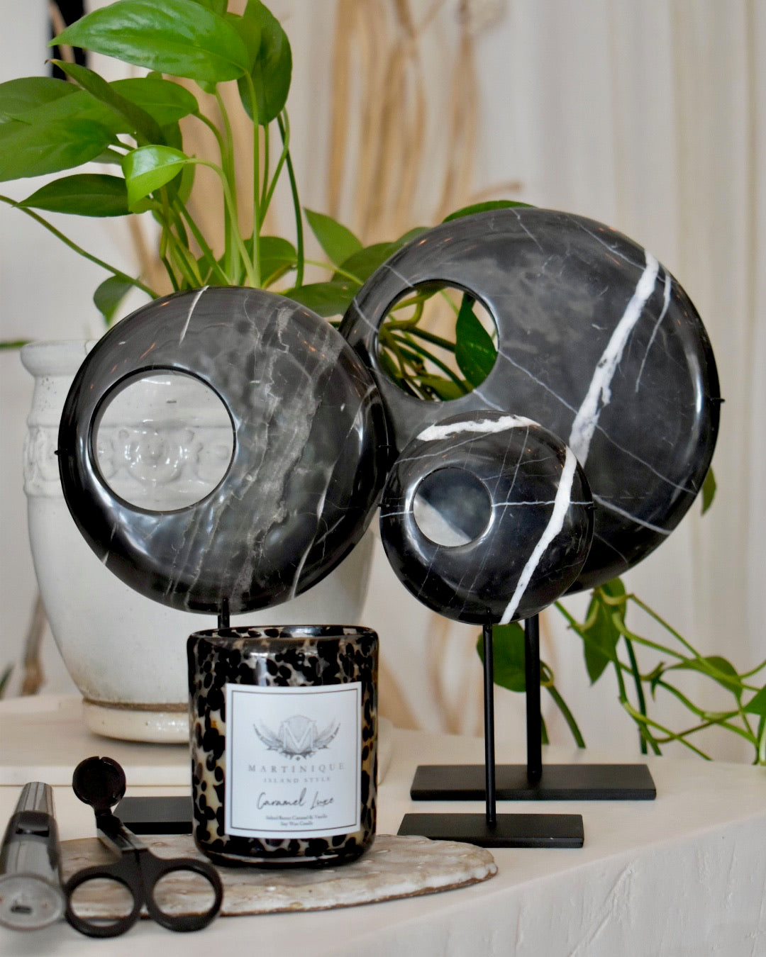 Decorative black marble sculptures on stands with a candle and scissors on a surface.