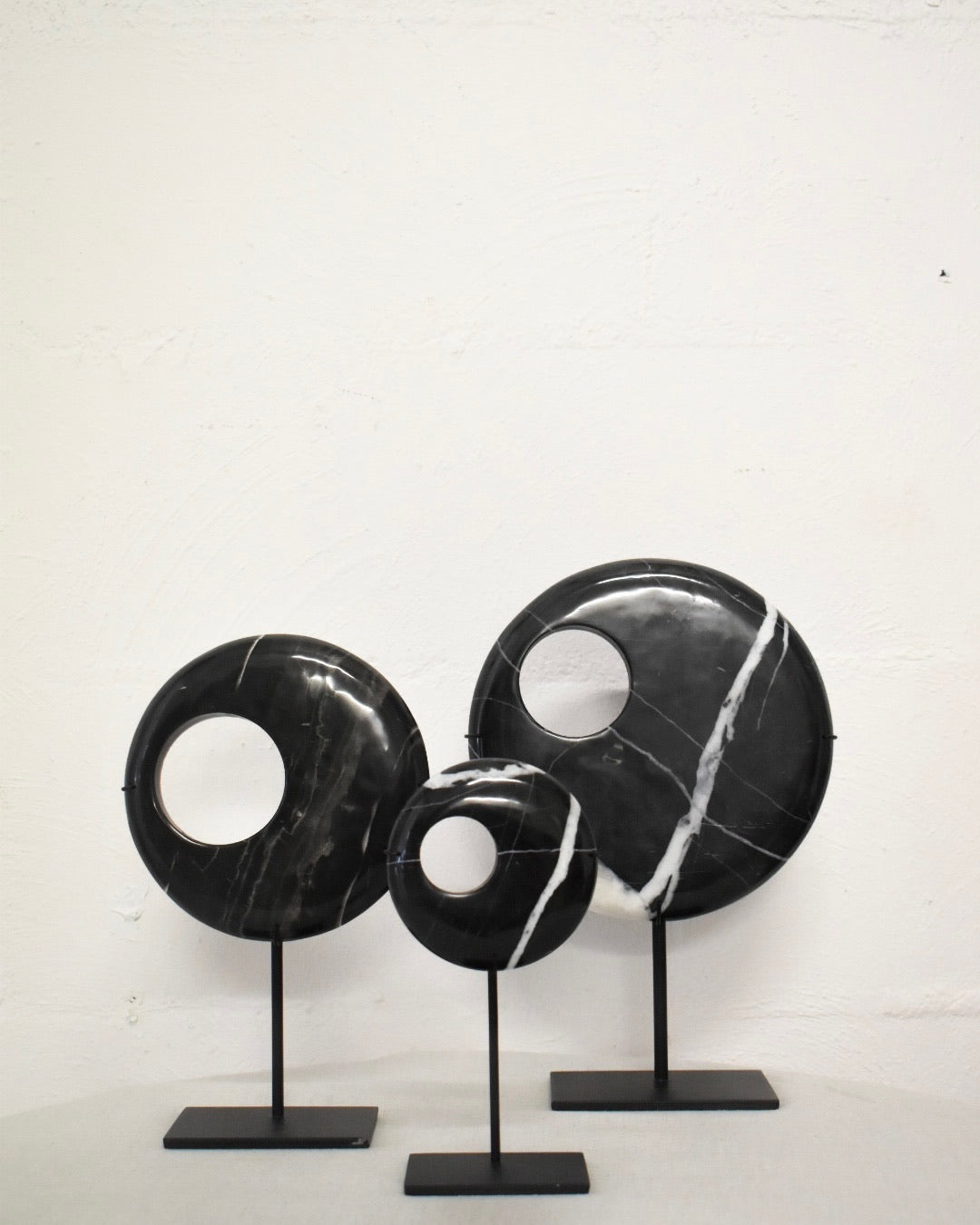 Black marble decorative pieces on stands against a white background