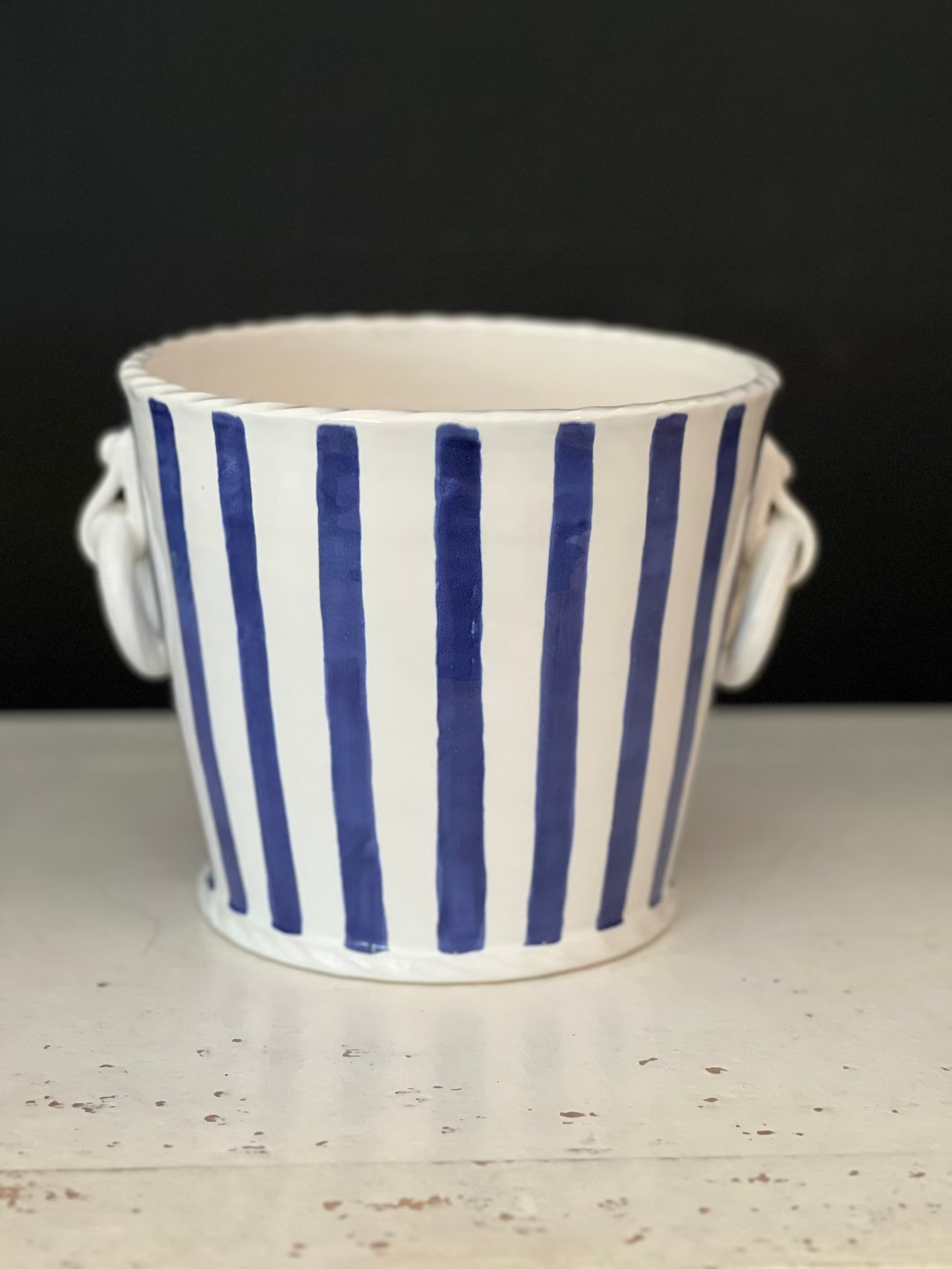Ceramic planter with blue and white stripes on a speckled surface with black background