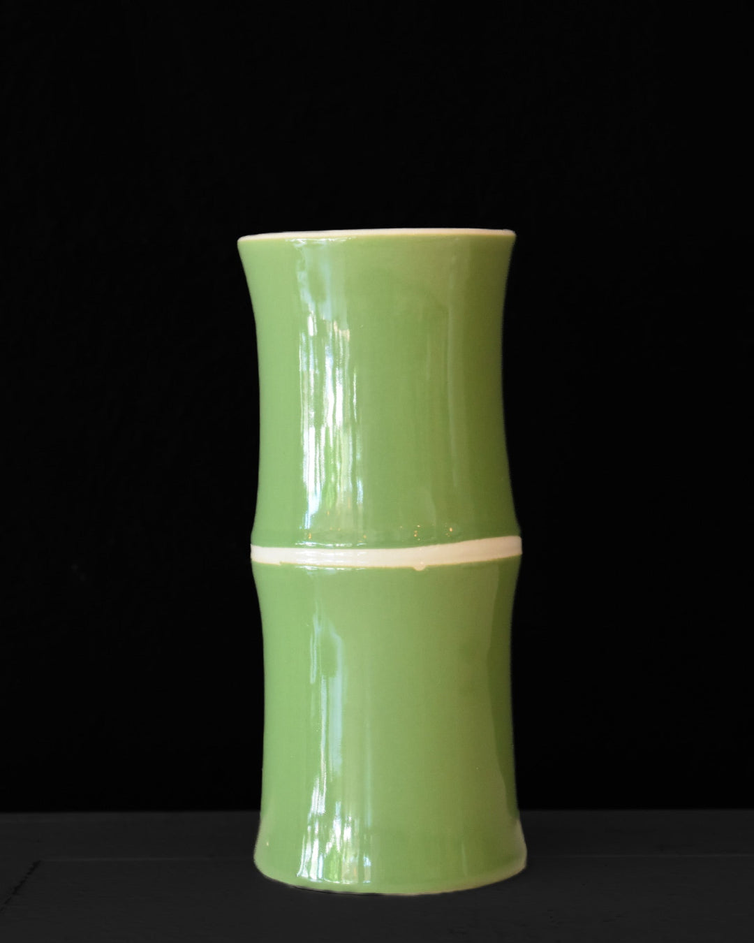 Green ceramic vase with a ribbed texture on a black background