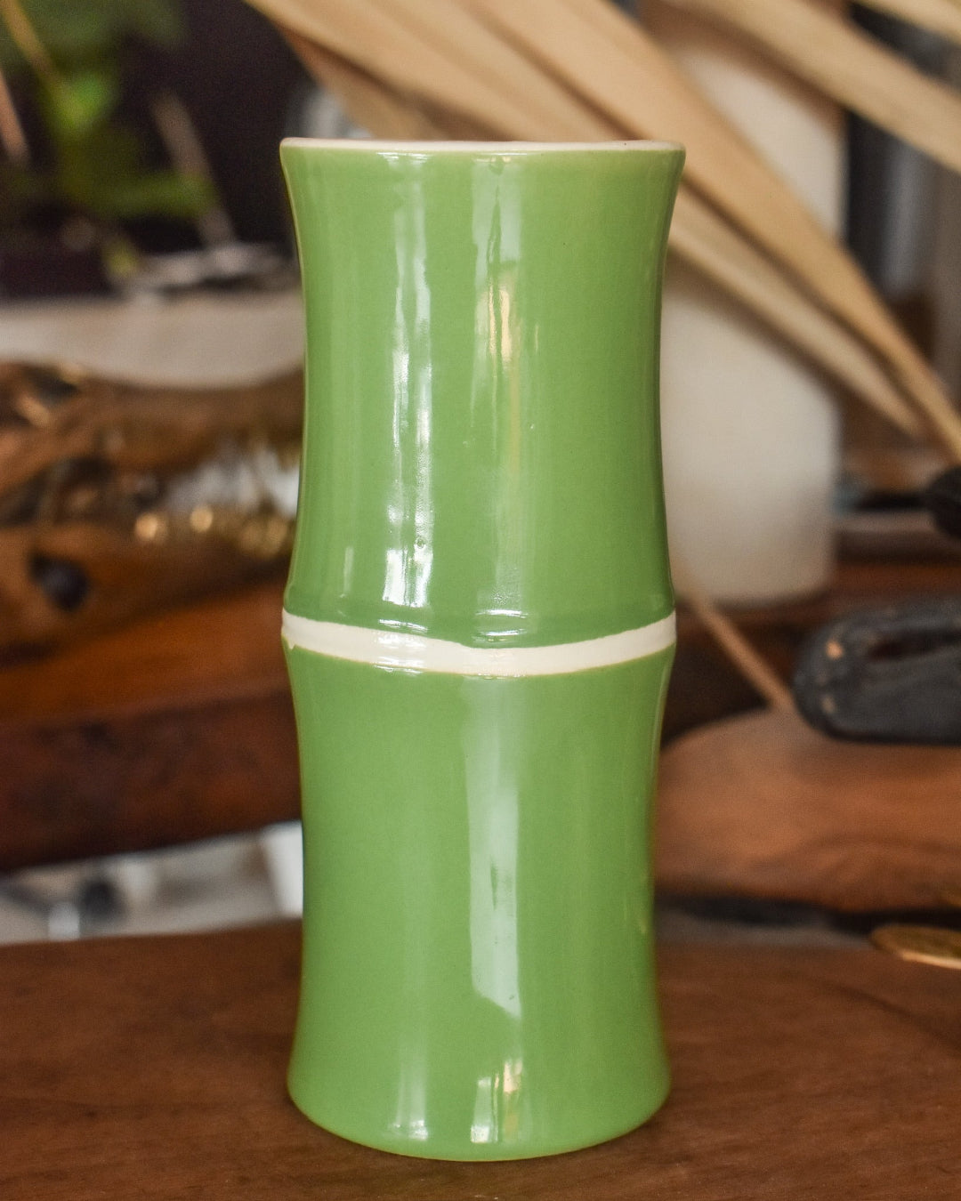 Green ceramic vase with a white stripe on a wooden surface