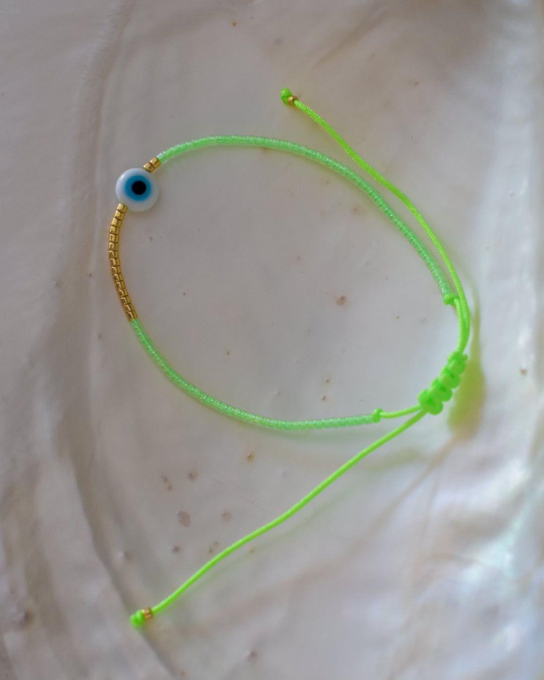Green bracelet with a small blue and white eye charm on a beige background