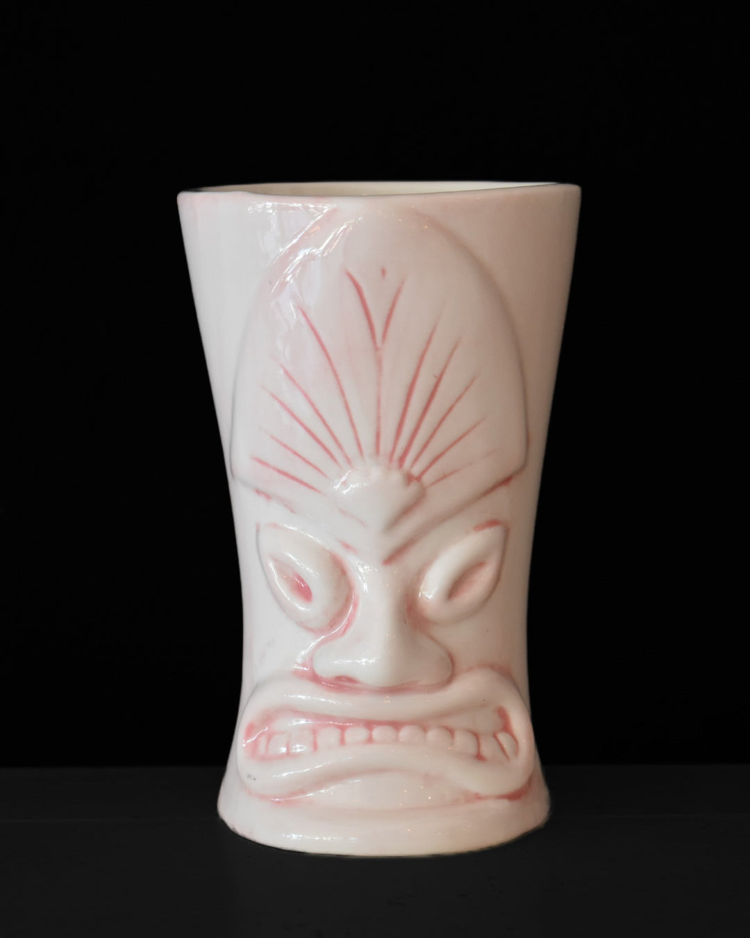 Pink tiki mug with a face design on a black background