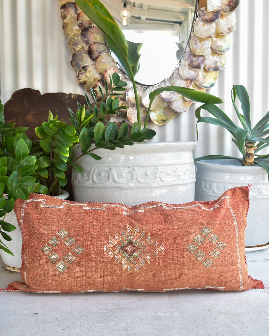 Decorative pillow with geometric patterns on a surface with plants and a mirror in the background