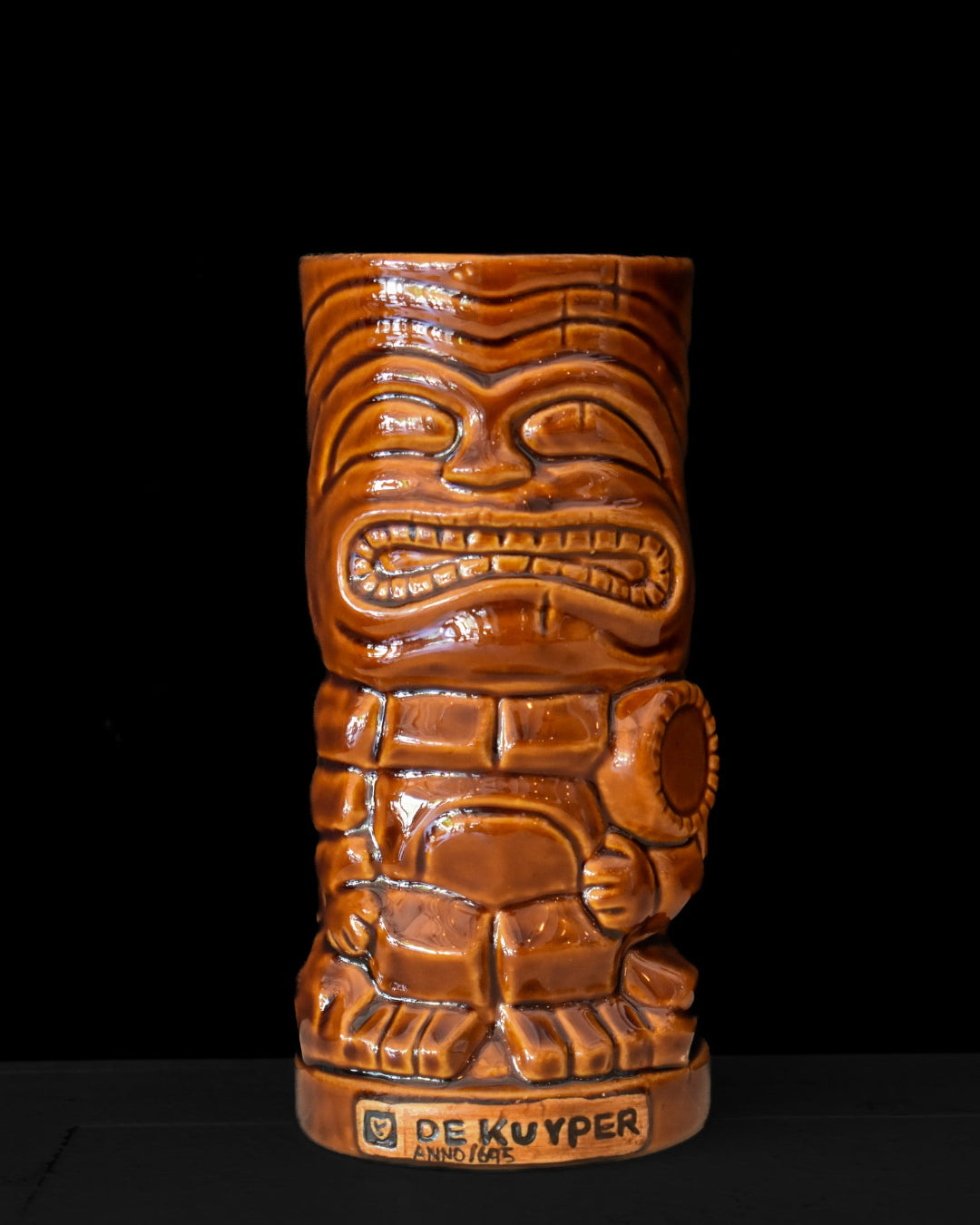 Brown tiki mug with intricate carvings on a black background