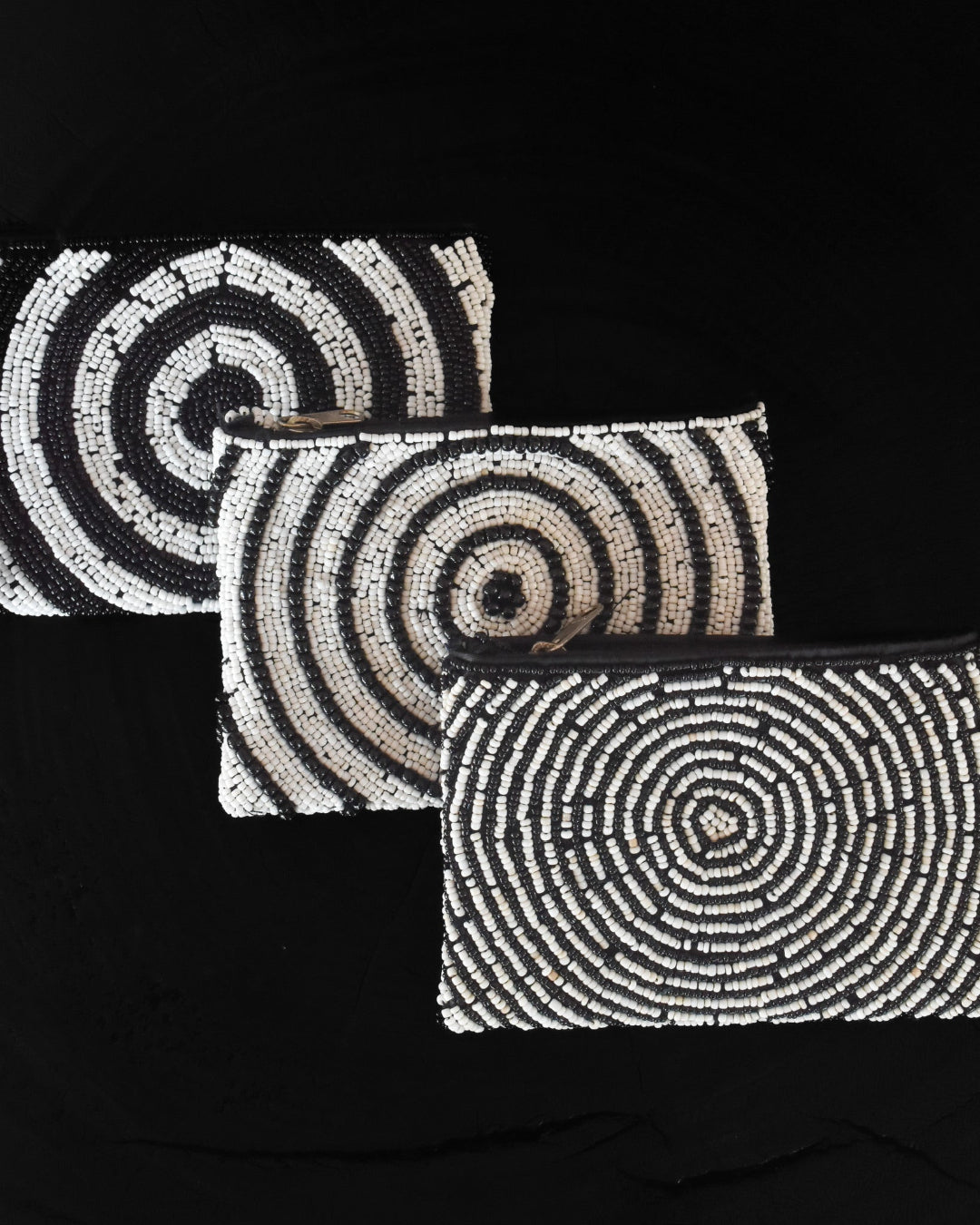 Set of three black and white beaded clutch bags on a black background