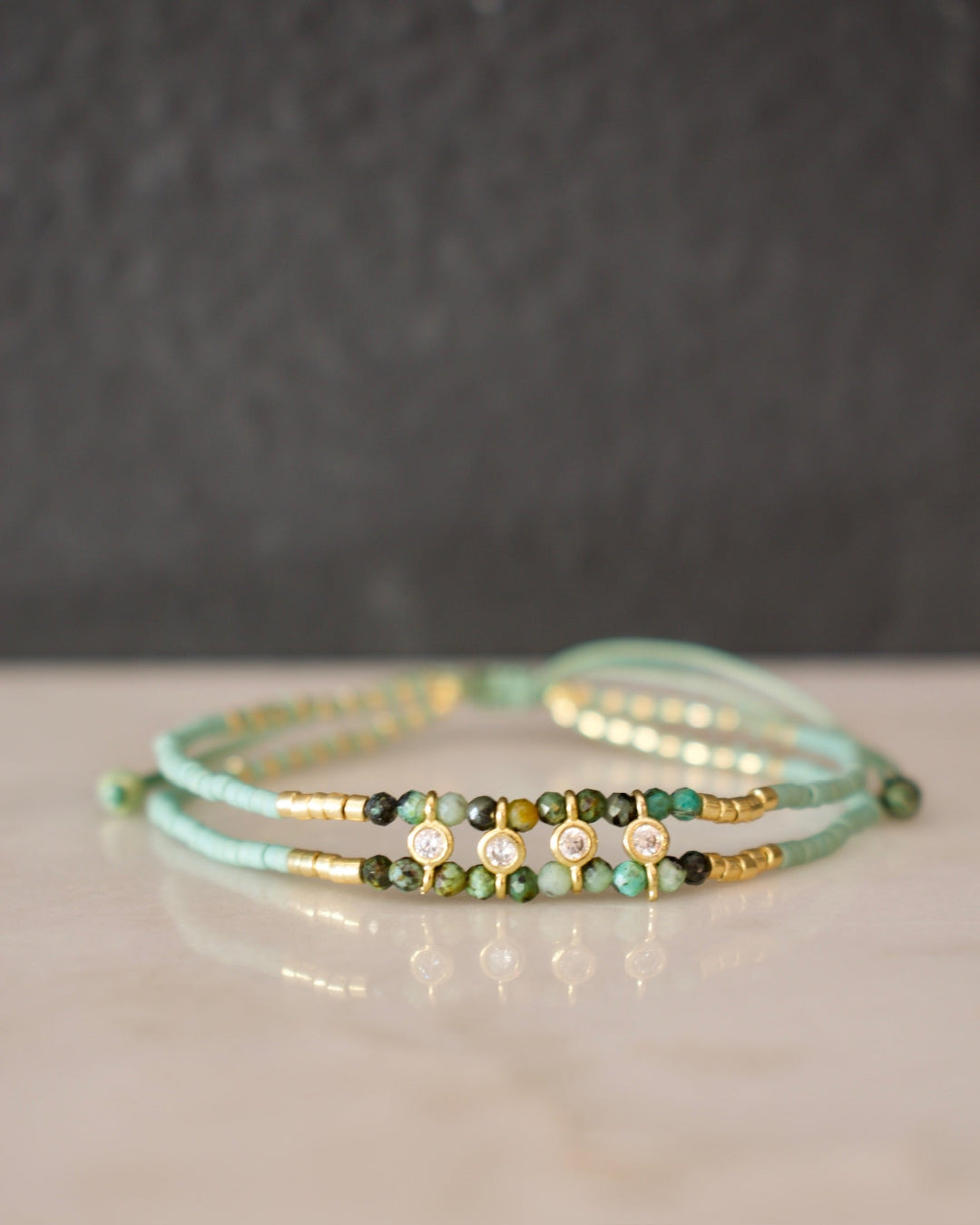 Set of three beaded bracelets on a reflective surface with a dark background