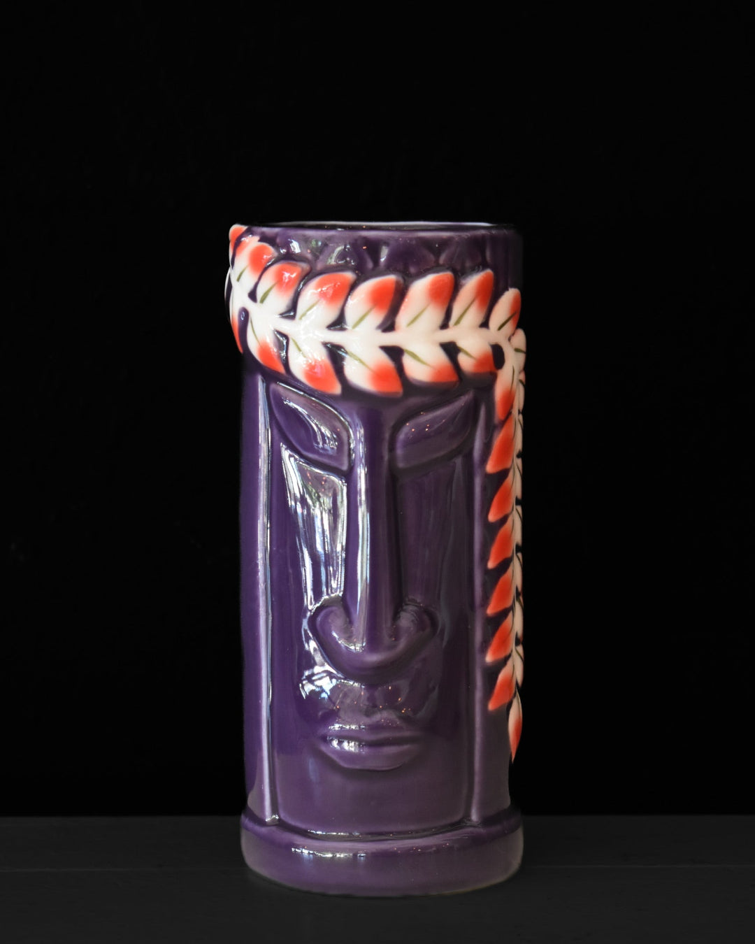 Purple tiki mug with orange and white designs on a black background