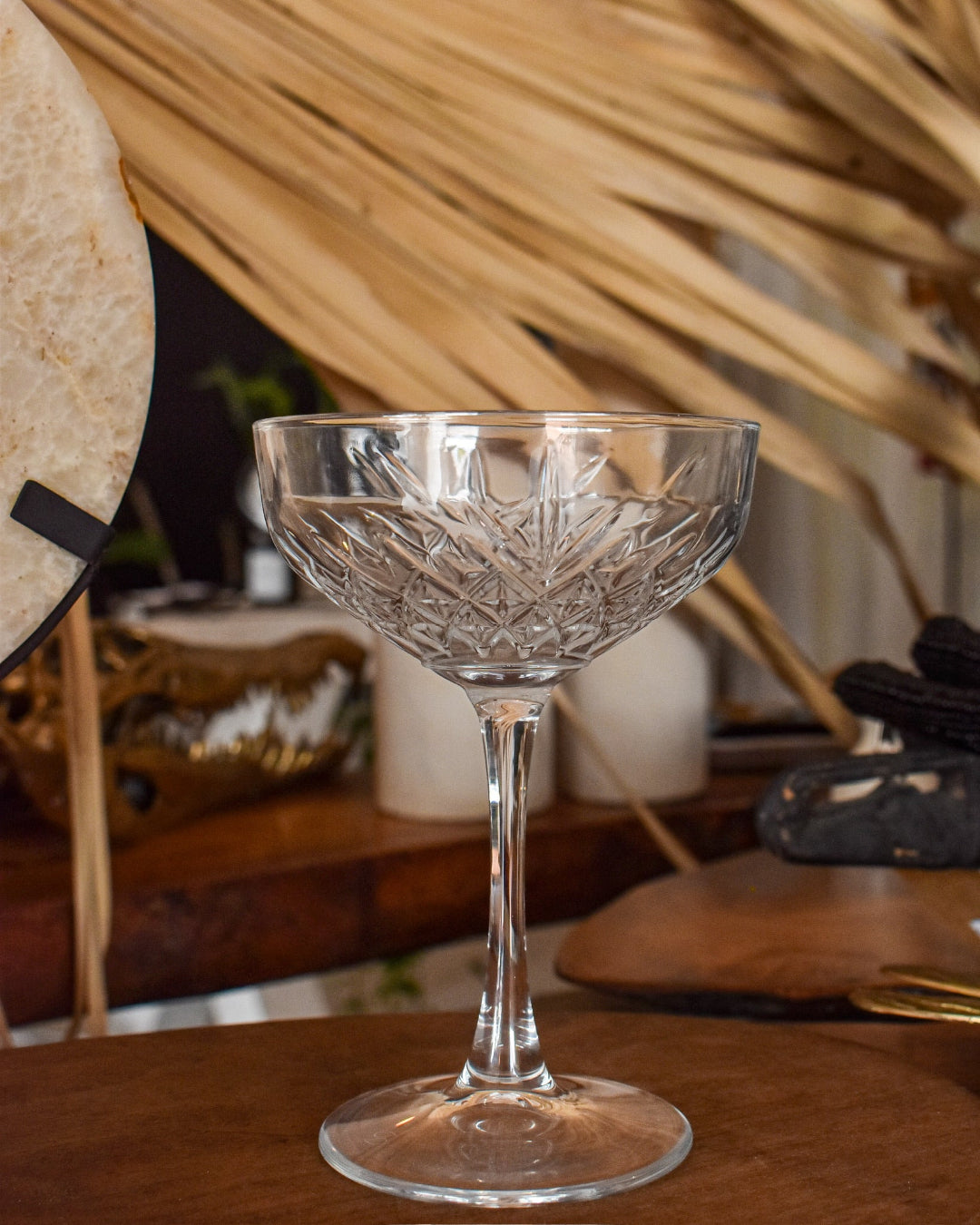 Clear glass coupe on a wooden surface with decorative elements in the background