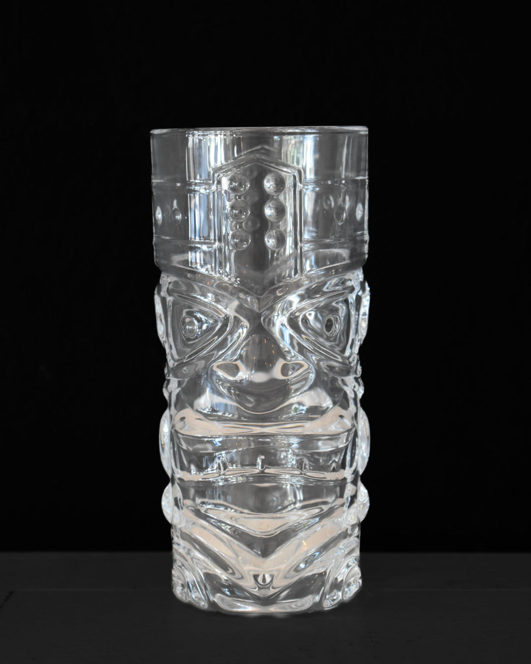 Clear glass tiki mug with intricate designs on a black background